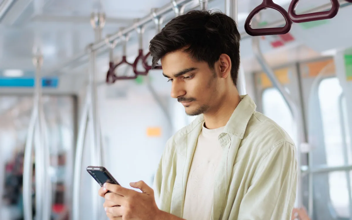 A young man stands on the train looking at his phone